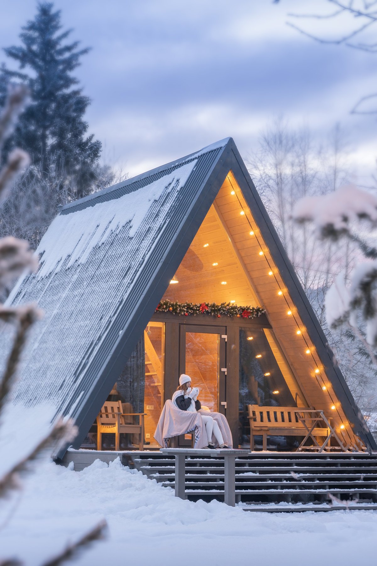 A-frame cabin with a steep snow-covered roof in a winter forest