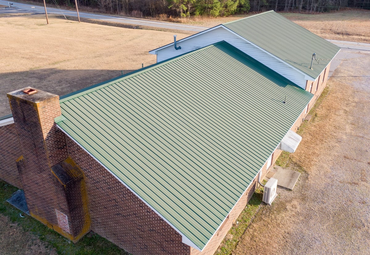 Forest green standing seam metal roof seen from above, with ridge cap and pipe penetrations
